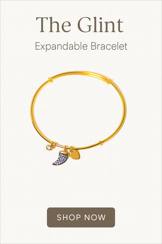 Gold expandable bracelet with charms on a white background, featuring 'The Glint' brand.